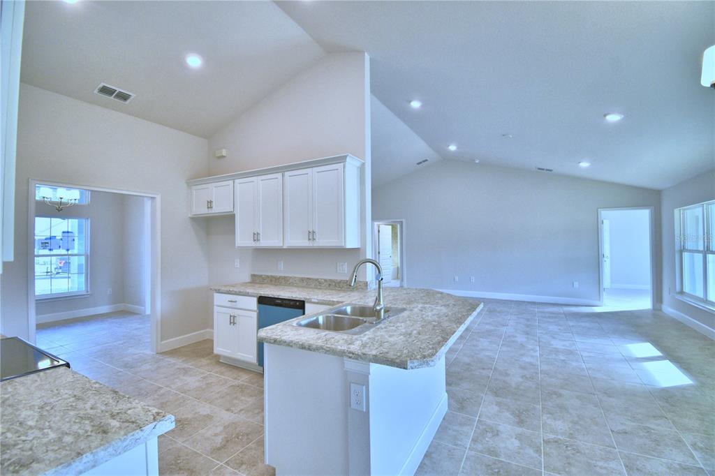 A kitchen with white cabinets, granite countertops, and tile flooring opens into a living area — 4429 JUNEBERRY DRIVE, AUBURNDALE, FL