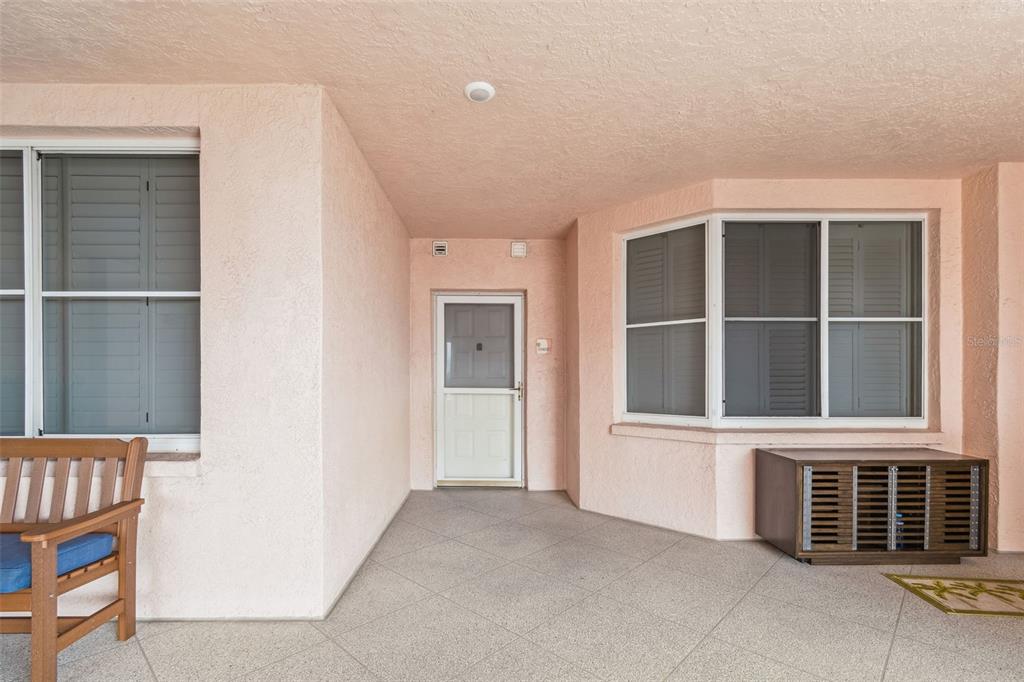 A covered patio features pink stucco walls, a tiled floor, and a wooden bench — 4991 BACOPA LANE S UNIT 502, ST PETERSBURG, FL