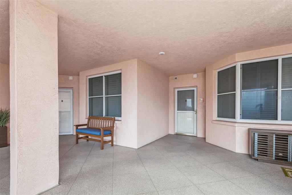 A covered outdoor patio features light pink stucco walls, tile flooring, and a wooden bench — 4991 BACOPA LANE S UNIT 502, ST PETERSBURG, FL