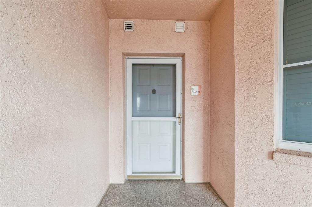 A front entryway features a white storm door, textured pink walls, and a tiled floor — 4991 BACOPA LANE S UNIT 502, ST PETERSBURG, FL