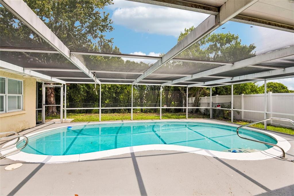 A kidney-shaped swimming pool is enclosed by a screened-in lanai with a concrete deck — 7303 HEATH DRIVE, PORT RICHEY, FL