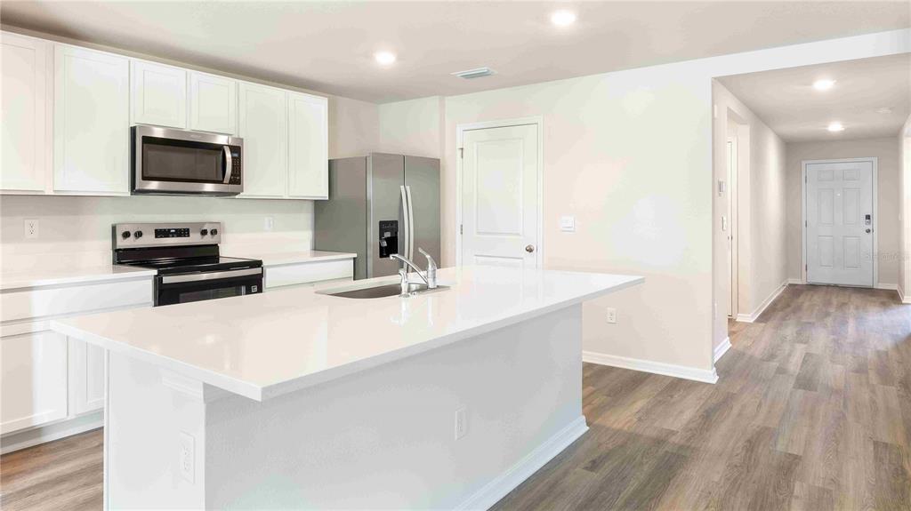 A modern kitchen features white cabinets, stainless steel appliances, and a large white island — 11908 MOUNTAIN ISLAND TRAIL, PARRISH, FL