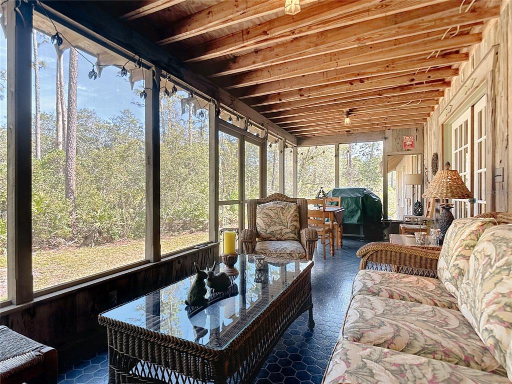 A screened-in porch with wicker furniture, a glass-top coffee table, and exposed wooden ceiling beams — 3939 LAKE ERIE ROAD, GROVELAND, FL