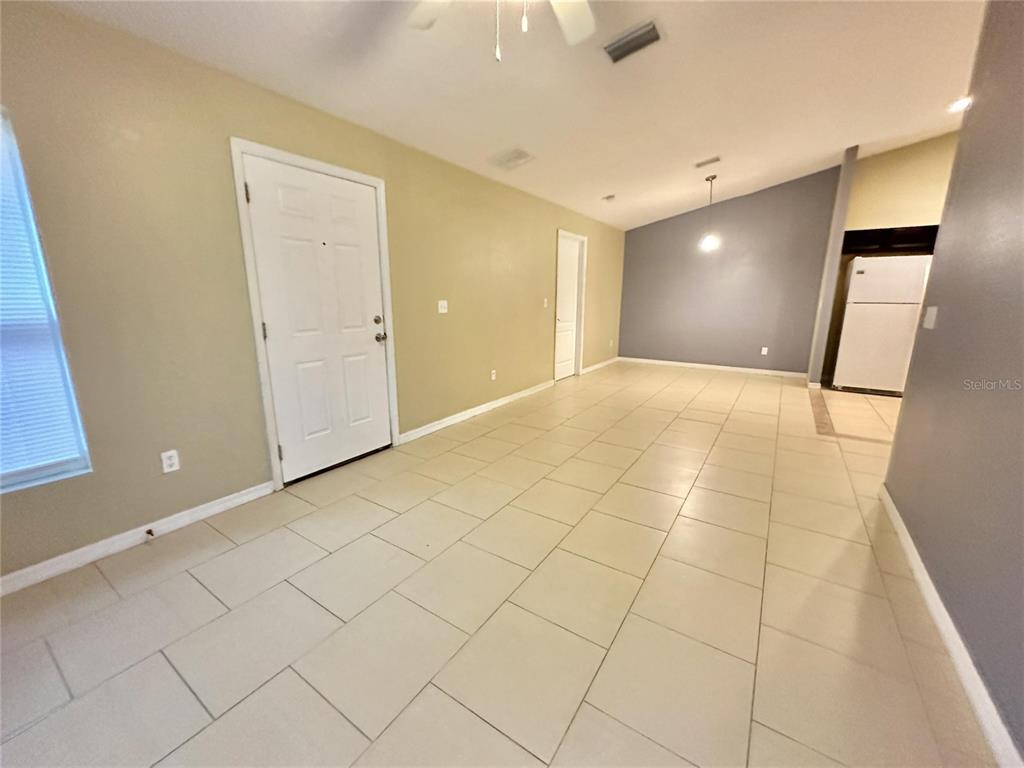 An open-concept room features light-colored tile flooring, beige walls, and a white entry door — 1013 KING STREET UNIT 1013, KISSIMMEE, FL