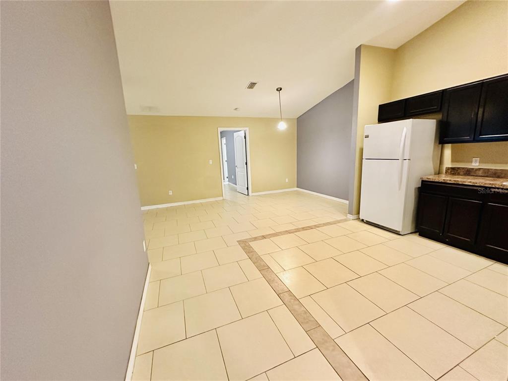 A kitchen with dark cabinets and a white refrigerator opens into a tiled dining area — 1013 KING STREET UNIT 1013, KISSIMMEE, FL