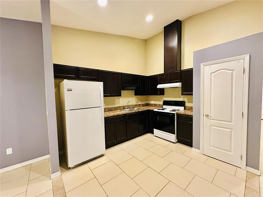 A kitchen features dark wood cabinets, white appliances, and light-colored tile flooring — 1013 KING STREET UNIT 1013, KISSIMMEE, FL