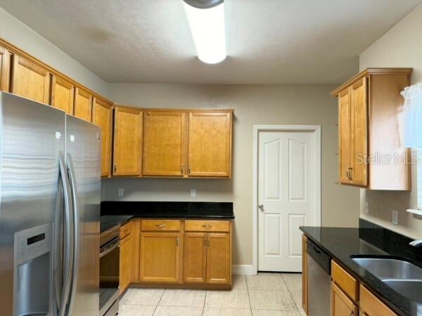 A kitchen features light wood cabinets, black countertops, stainless steel appliances, and tile flooring — 8992 SW 79TH AVENUE, GAINESVILLE, FL