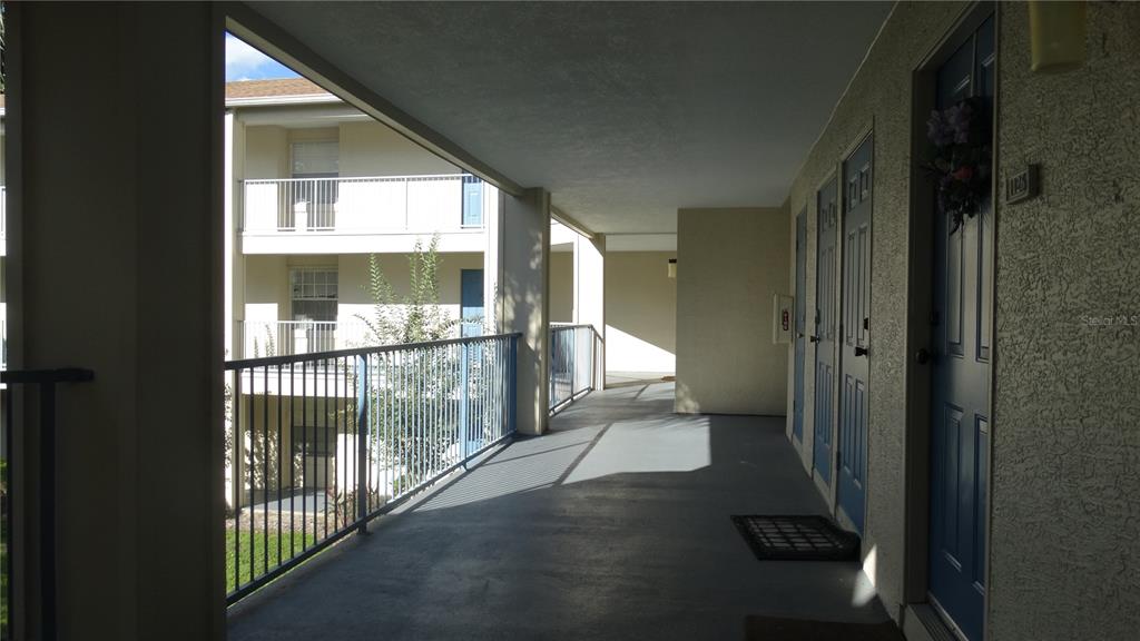 An outdoor apartment walkway features blue doors, a metal railing, and a concrete floor — 7240 WESTPOINTE BOULEVARD UNIT 1125, ORLANDO, FL