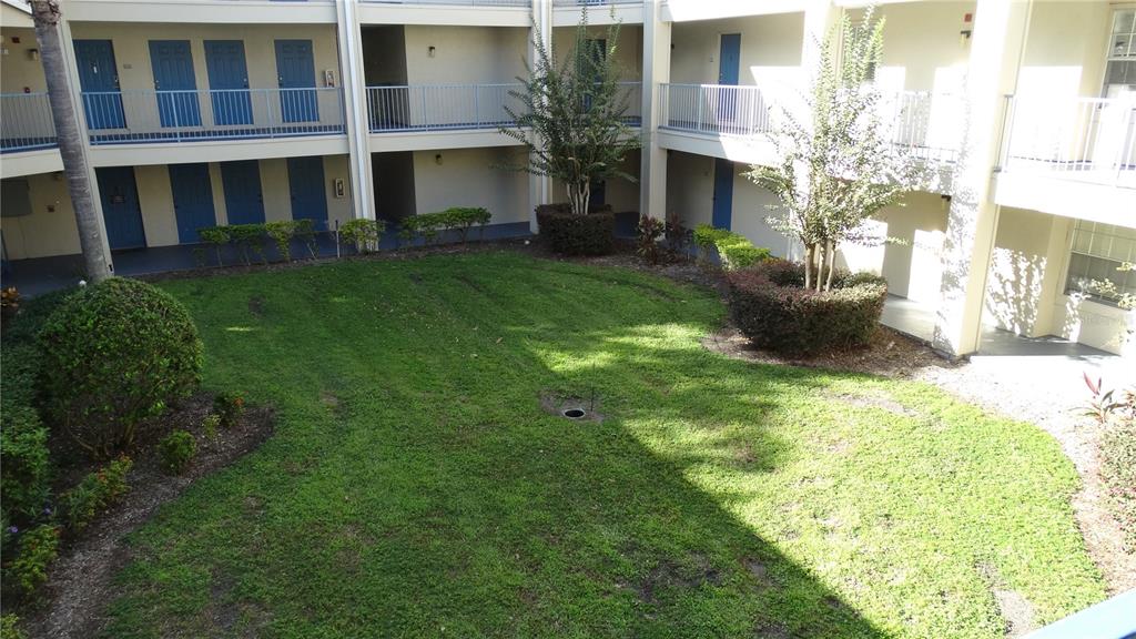 A grassy courtyard is surrounded by a multi-story apartment building with blue doors — 7240 WESTPOINTE BOULEVARD UNIT 1125, ORLANDO, FL