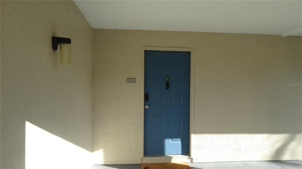 A blue front door with a house number is set into a beige stucco wall — 7240 WESTPOINTE BOULEVARD UNIT 1125, ORLANDO, FL