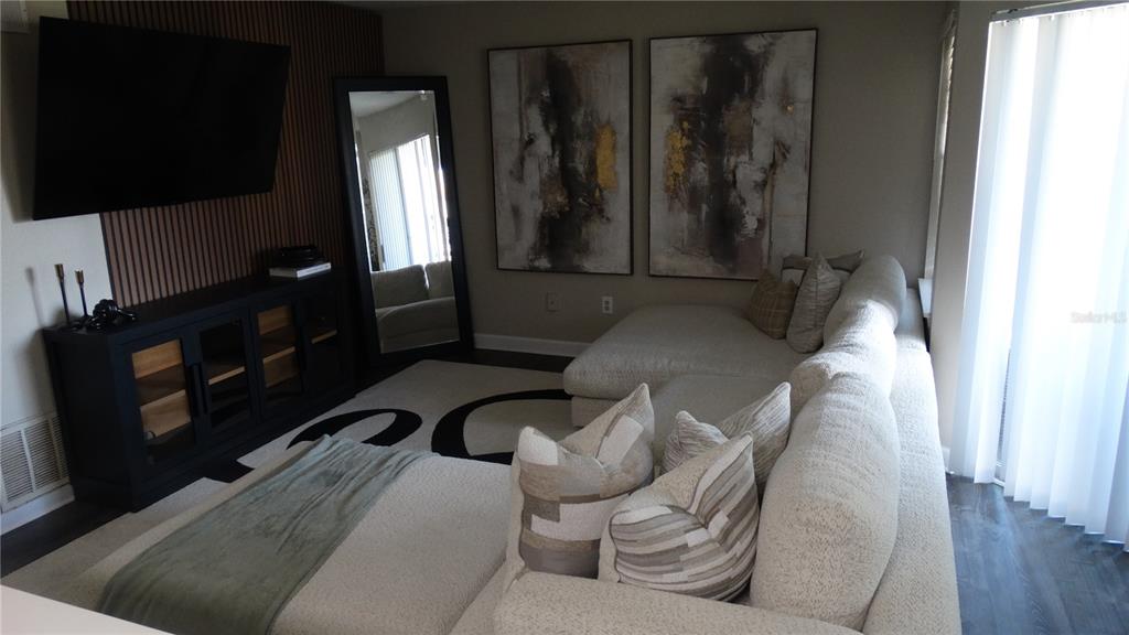 A living room features a large sectional sofa, a wall-mounted television, and abstract wall art — 7240 WESTPOINTE BOULEVARD UNIT 1125, ORLANDO, FL