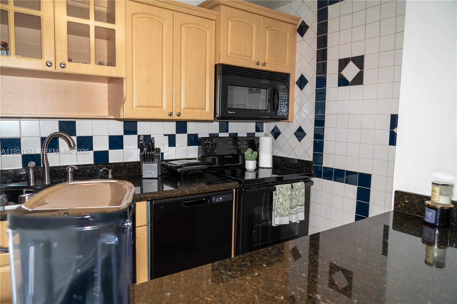 A kitchen features light wood cabinets, black appliances, dark granite countertops, and a checkered tile backsplash — 854 NW 87th Ave # 405, Miami FL 33172, MIAMI, FL
