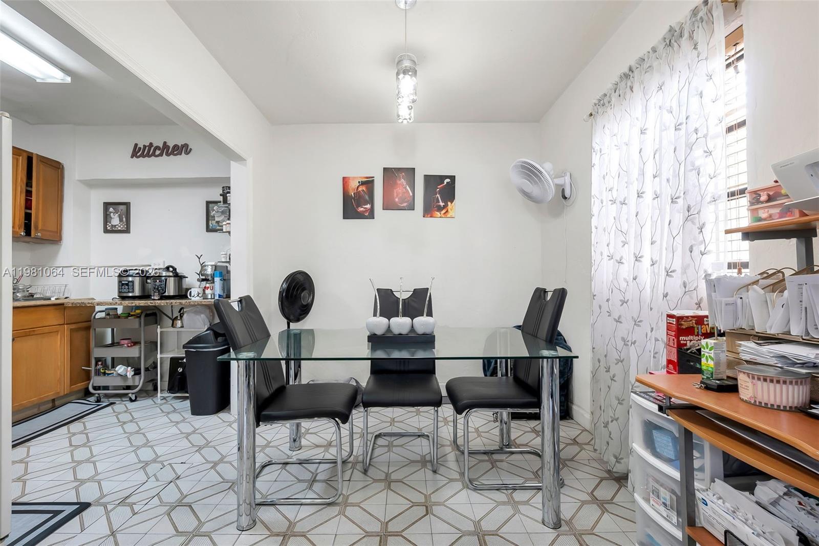 A dining area with a glass table, black chairs, and tile flooring adjacent to a kitchen — 3250 NW 14th Ter, Miami FL 33125, MIAMI, FL
