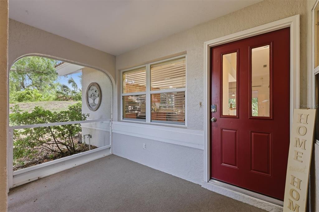 A covered front porch features a red door, a window, and a white railing — 4461 ASCOT CIRCLE N, SARASOTA, FL