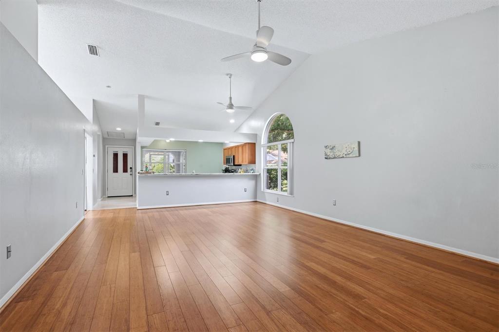 A spacious living room with vaulted ceilings, wood flooring, and an open kitchen pass-through — 4461 ASCOT CIRCLE N, SARASOTA, FL