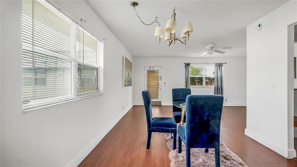 A dining room features blue velvet chairs, a glass table, wood floors, and a chandelier — 703 Brittany # O, Delray Beach FL 33446, DELRAY BEACH, FL