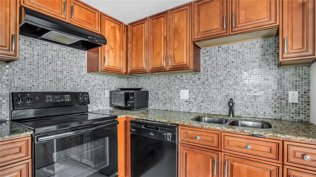 A kitchen features wood cabinets, granite countertops, a black stove, and a mosaic tile backsplash — 703 Brittany # O, Delray Beach FL 33446, DELRAY BEACH, FL