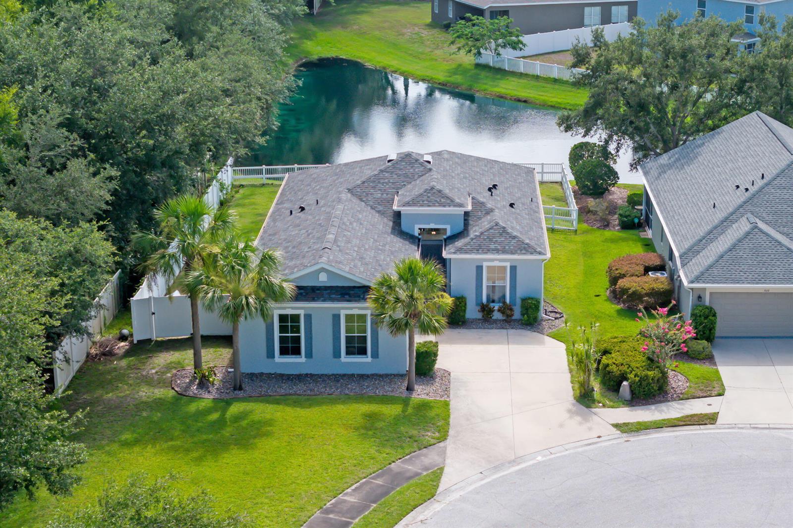 An aerial view shows a light blue house with a gray roof, palm trees, and pond — 7005 56th Terrace E, FL 34221, FL