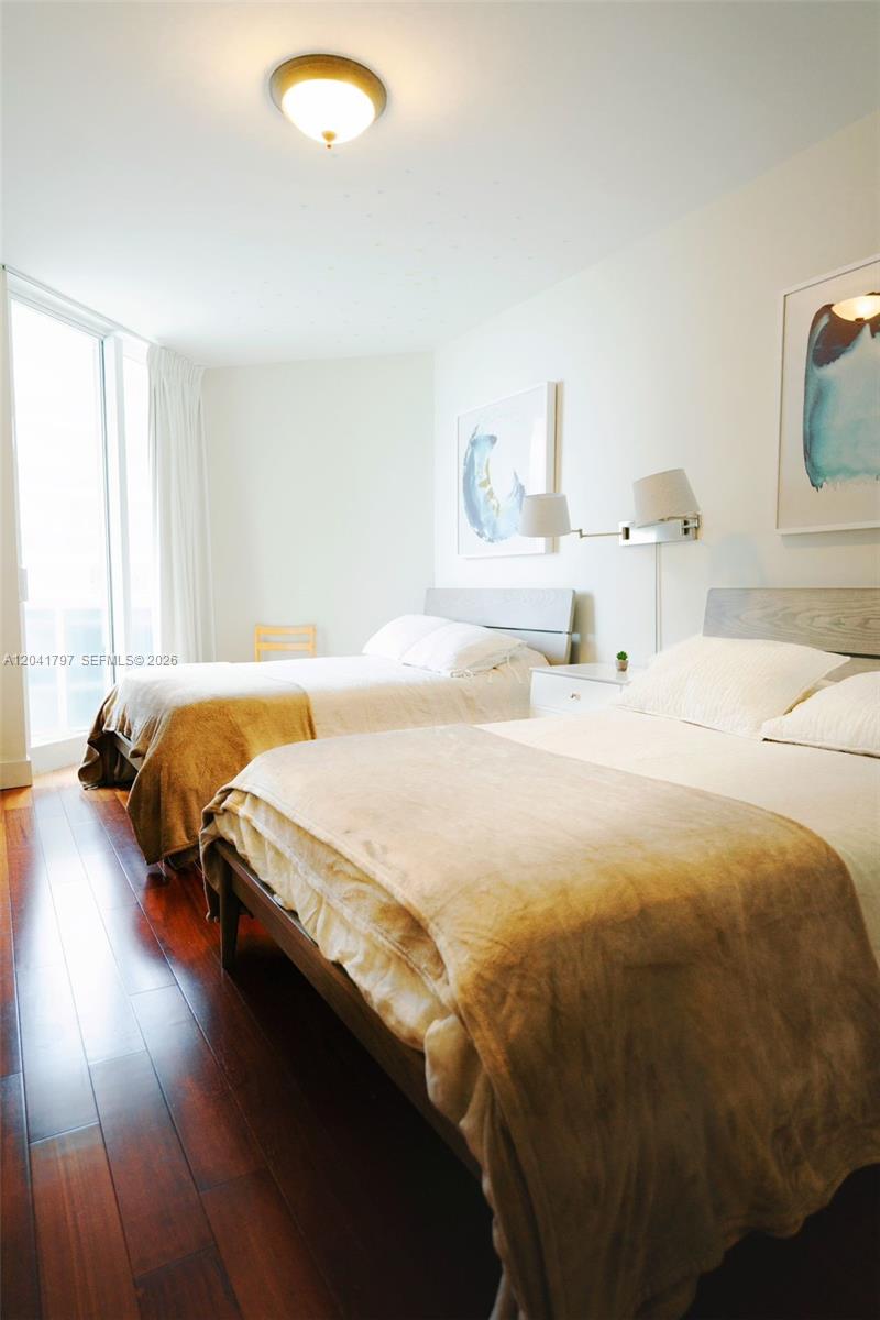 A bedroom features two beds, dark wood flooring, and a large window with white curtains — 9595 Collins Ave # C, Surfside FL 33154, SURFSIDE, FL