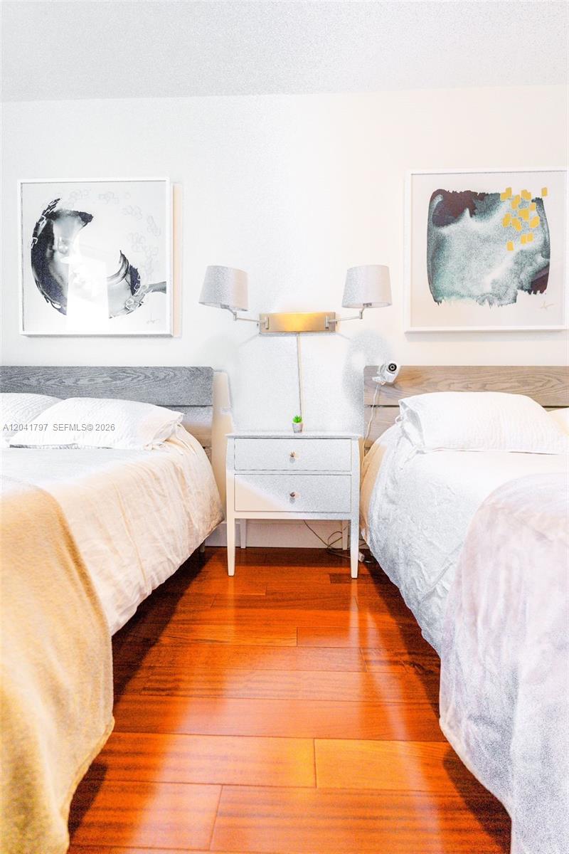 A bedroom features two beds separated by a white nightstand with a wall-mounted lamp — 9595 Collins Ave # C, Surfside FL 33154, SURFSIDE, FL