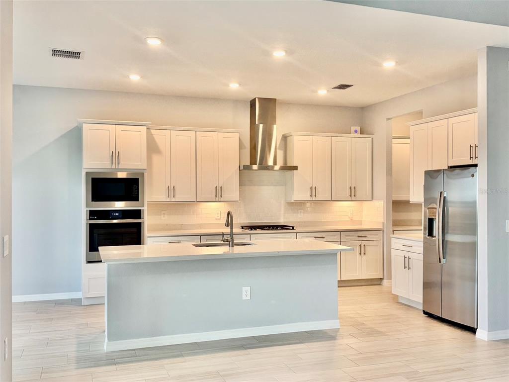 A modern kitchen features white cabinetry, stainless steel appliances, a center island, and light flooring — 19227 SCALLOP LOOP, LAKEWOOD RANCH, FL