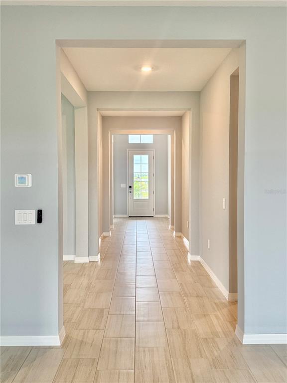 A long hallway with light-colored tile flooring leads toward a white front door — 19227 SCALLOP LOOP, LAKEWOOD RANCH, FL