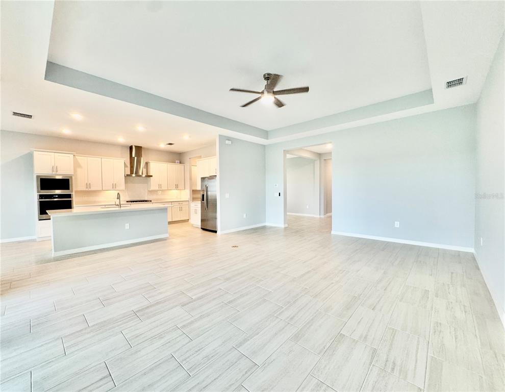 An open-concept kitchen and living area featuring light-colored tile flooring and a tray ceiling — 19227 SCALLOP LOOP, LAKEWOOD RANCH, FL