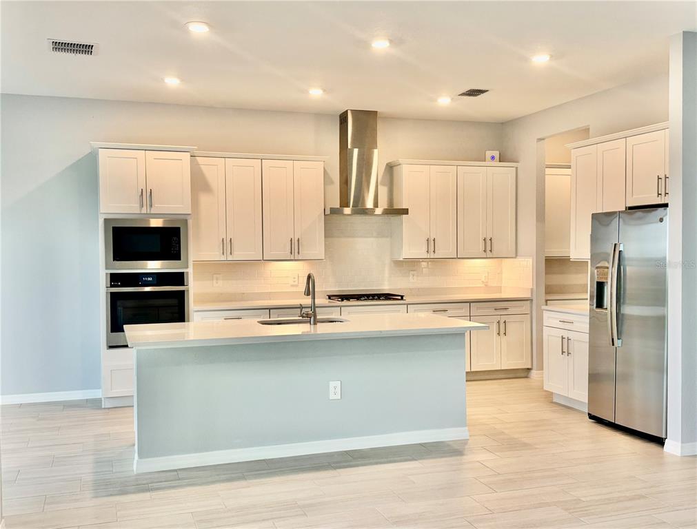 A modern kitchen features white cabinets, stainless steel appliances, a center island, and tile flooring — 19227 SCALLOP LOOP, LAKEWOOD RANCH, FL