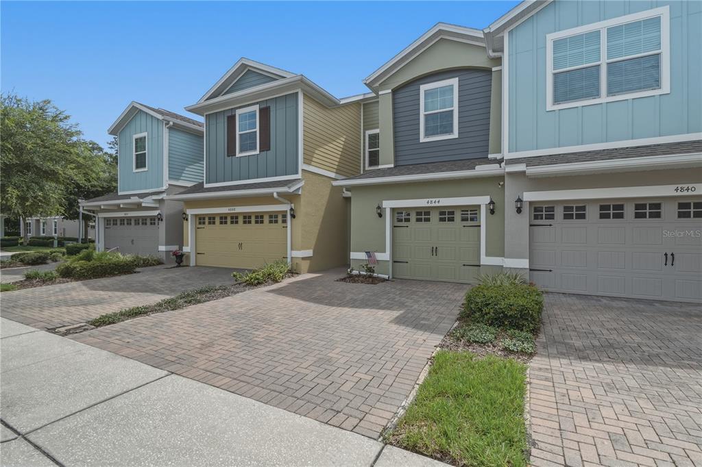 A row of multi-story townhomes with paved driveways and attached garages under a clear sky — 4844 CLIVEDEN LOOP, SANFORD, FL