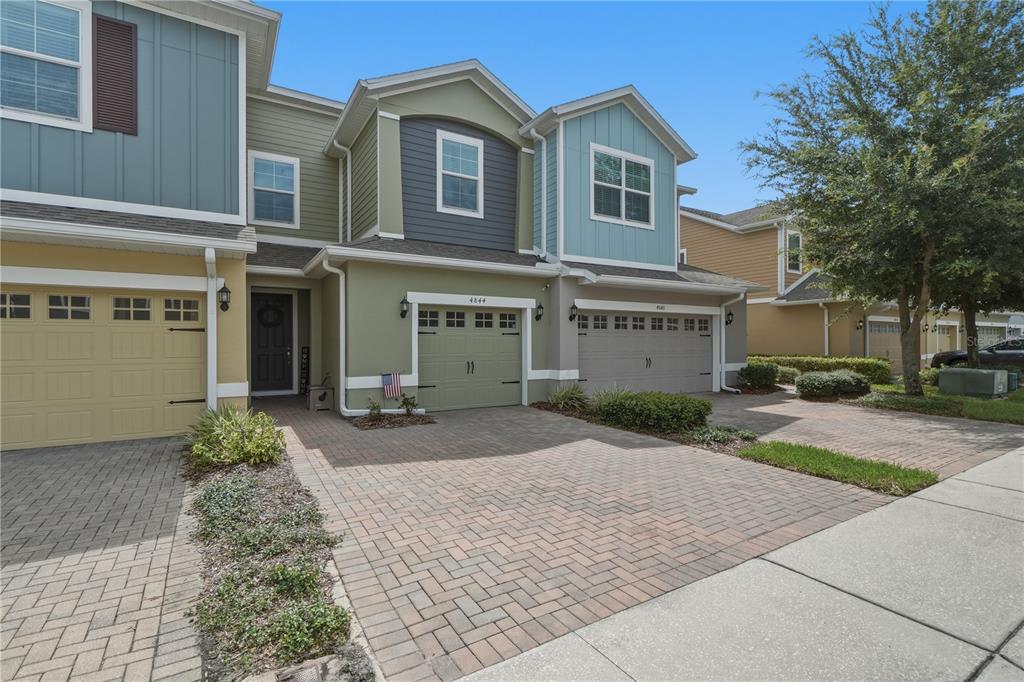A multi-story townhouse exterior features a brick driveway, two garage doors, and colorful siding — 4844 CLIVEDEN LOOP, SANFORD, FL