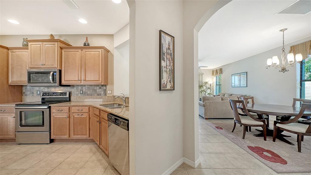 A kitchen with light wood cabinets and granite countertops opens into a dining area — 11109 CAMPAZZO DRIVE, VENICE, FL