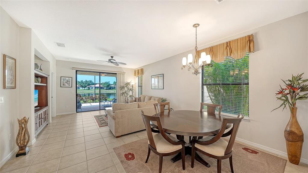 A dining area with a round table and chairs opens into a living room — 11109 CAMPAZZO DRIVE, VENICE, FL