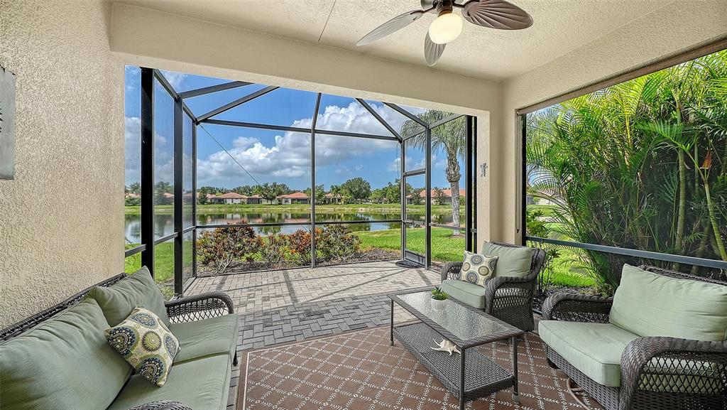 A screened-in patio features wicker furniture, a patterned rug, and a view of a lake — 11109 CAMPAZZO DRIVE, VENICE, FL