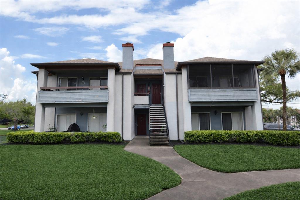 A two-story apartment building features a central staircase, balconies, and a manicured lawn — 10263 GANDY BOULEVARD N UNIT 414, ST PETERSBURG, FL