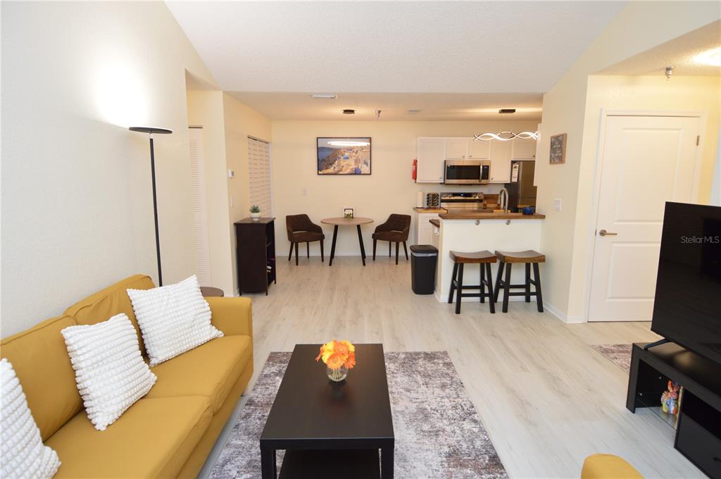 An open-concept living room and kitchen featuring a yellow sofa, dining area, and breakfast bar — 10263 GANDY BOULEVARD N UNIT 414, ST PETERSBURG, FL
