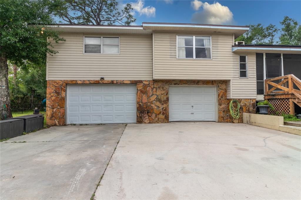 A two-story house features a stone-faced lower level with two garage doors and beige siding — 1143 MEYERS ROAD, VENICE, FL