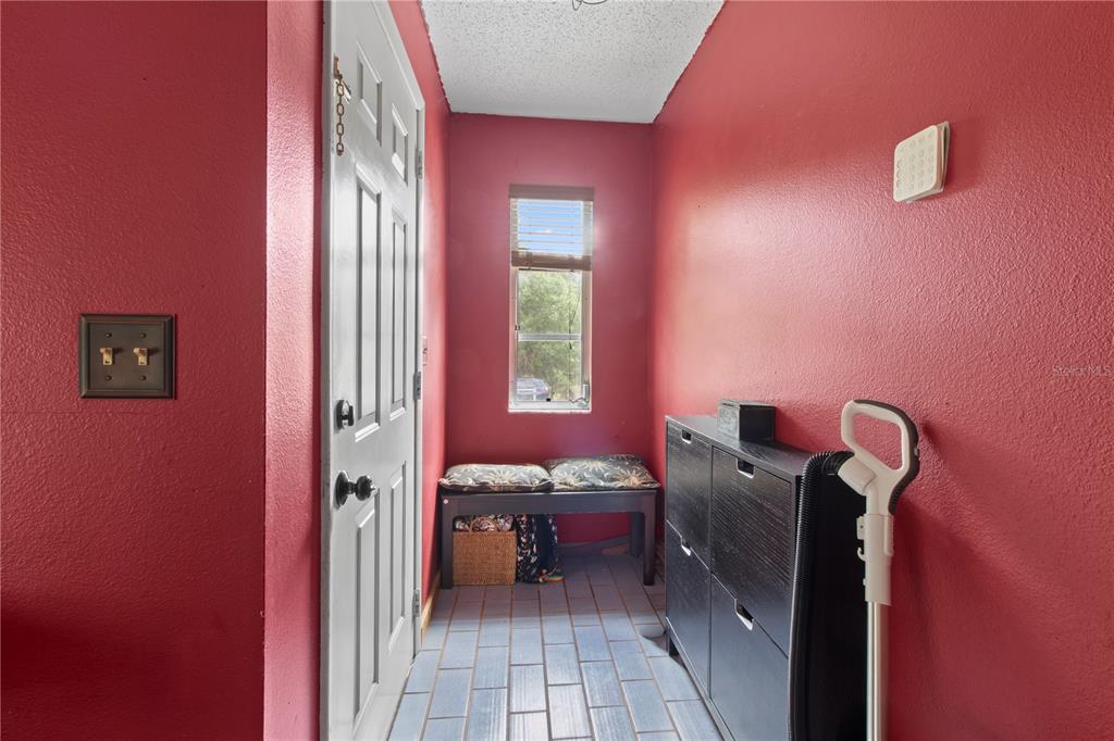 A narrow entryway features red walls, blue tiled flooring, a white door, and a bench — 1143 MEYERS ROAD, VENICE, FL