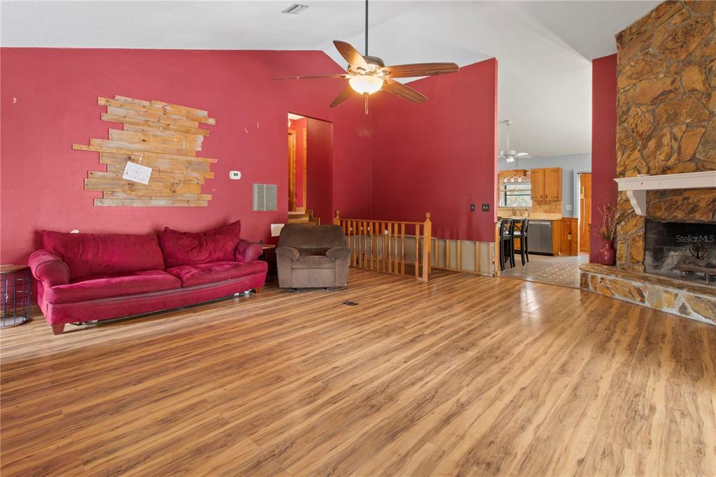 A living room features red walls, wood-look flooring, a stone fireplace, and a ceiling fan — 1143 MEYERS ROAD, VENICE, FL