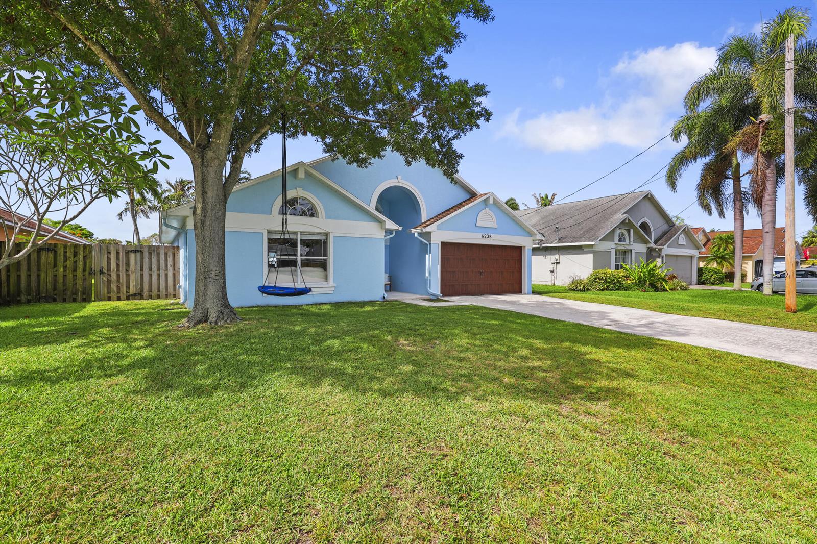 A light blue house with a brown garage door and a tree swing in front — 6238 Pompano Street, Jupiter FL 33458, JUPITER, FL