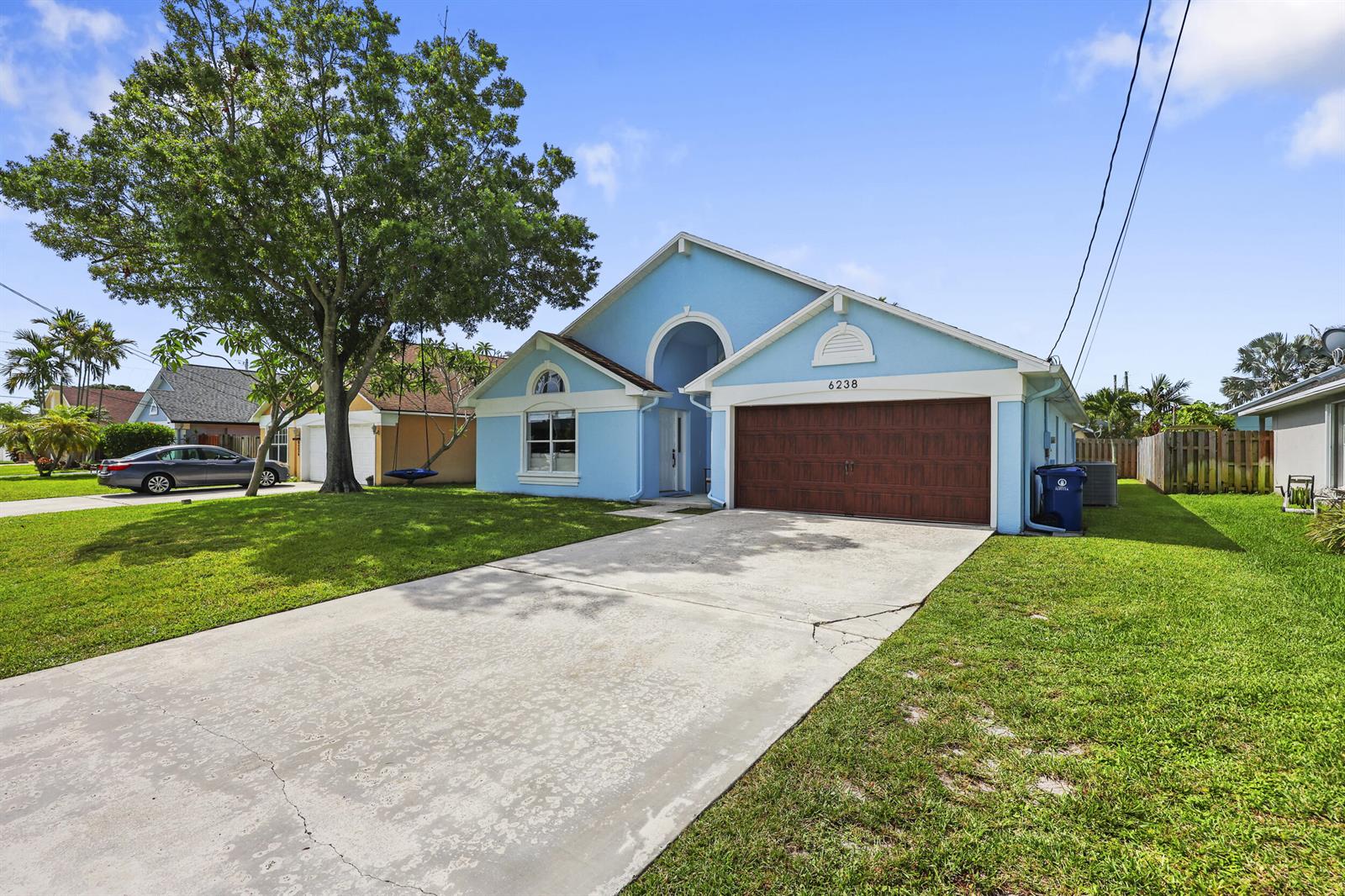 A light blue single-story house features a brown garage door and a concrete driveway — 6238 Pompano Street, Jupiter FL 33458, JUPITER, FL