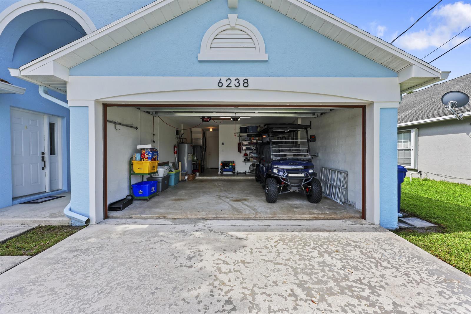 A blue house features an open garage containing a golf cart and storage items — 6238 Pompano Street, Jupiter FL 33458, JUPITER, FL