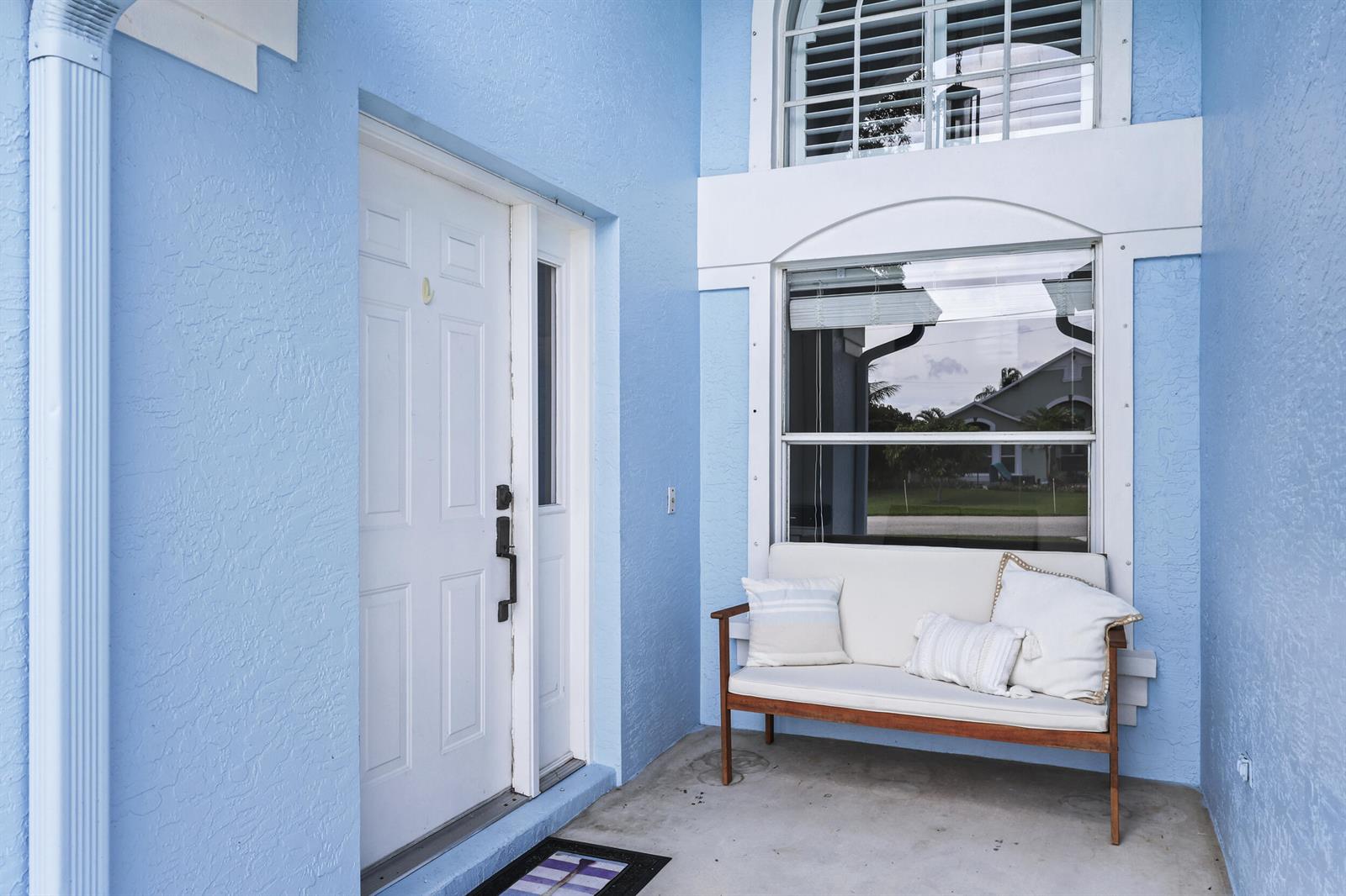 A light blue exterior entryway features a white front door, a window, and a wooden bench — 6238 Pompano Street, Jupiter FL 33458, JUPITER, FL