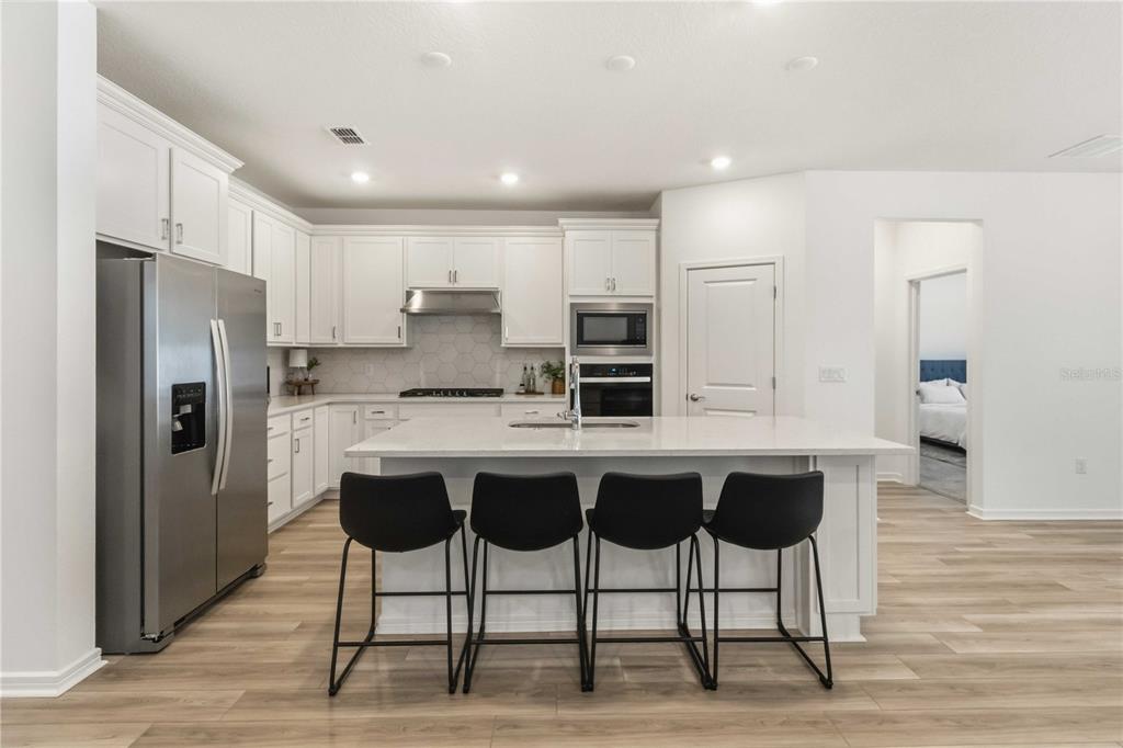 A modern kitchen features white cabinetry, a large center island with four stools, and stainless appliances — 2940 FOREST MEADOW AVENUE, VALRICO, FL