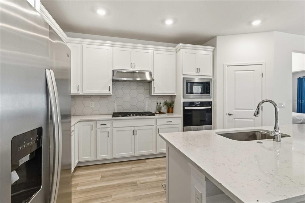 A modern kitchen features white cabinets, stainless steel appliances, a quartz island, and light flooring — 2940 FOREST MEADOW AVENUE, VALRICO, FL
