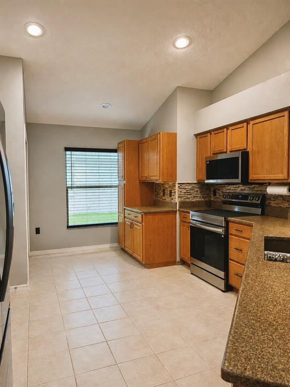 A kitchen features light-colored tile floors, oak cabinets, stainless steel appliances, and granite countertops — 4828 WESSEX WAY, LAND O LAKES, FL