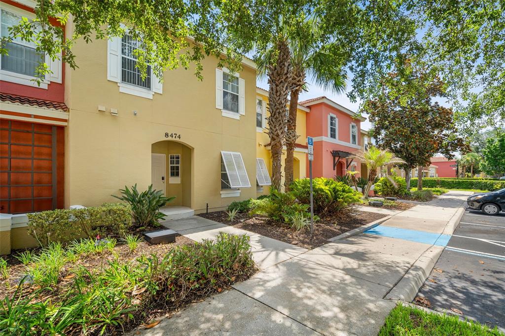 A two-story tan townhouse exterior with a front entrance, shutters, and a palm tree — 8474 CRYSTAL COVE LOOP, KISSIMMEE, FL