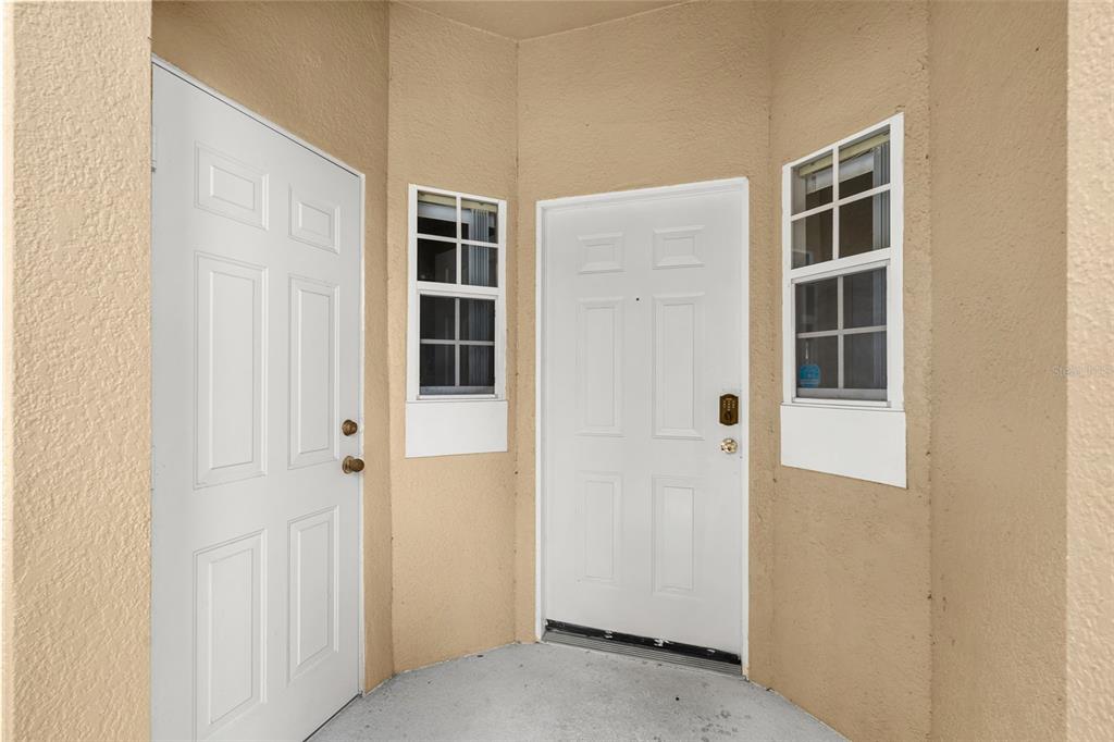 An exterior entryway features two white doors and two windows set into tan stucco walls — 8474 CRYSTAL COVE LOOP, KISSIMMEE, FL