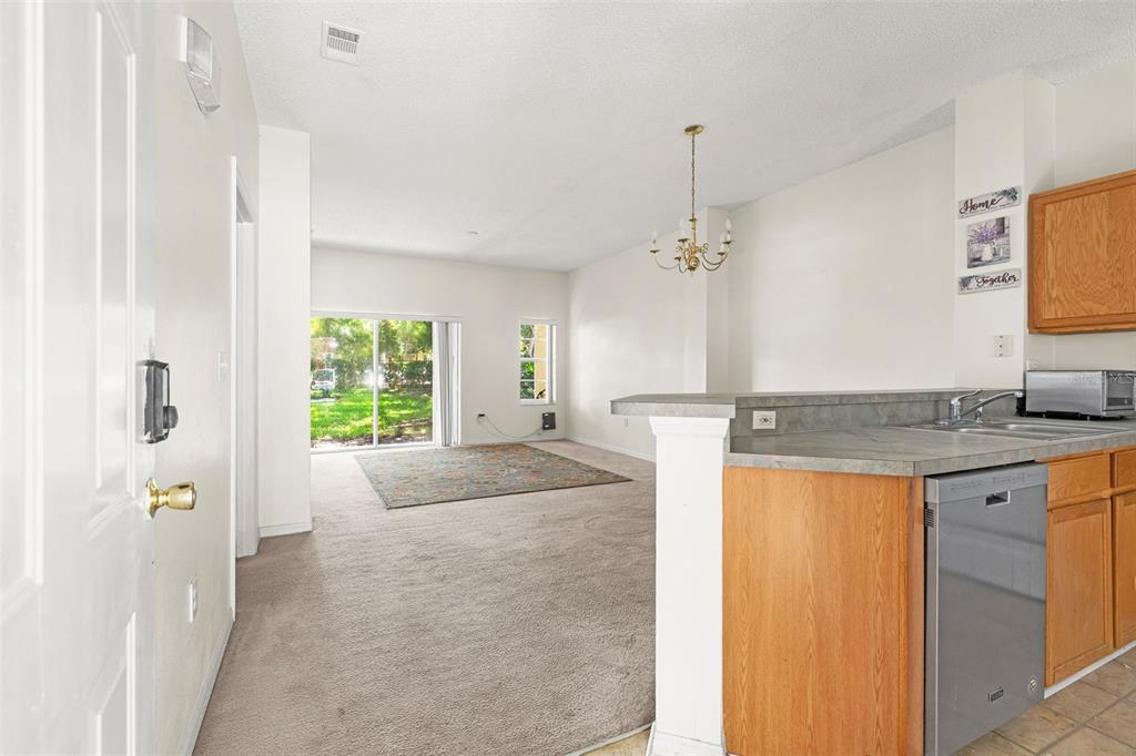 A view from a kitchen looking into a carpeted living area with sliding glass doors — 8474 CRYSTAL COVE LOOP, KISSIMMEE, FL