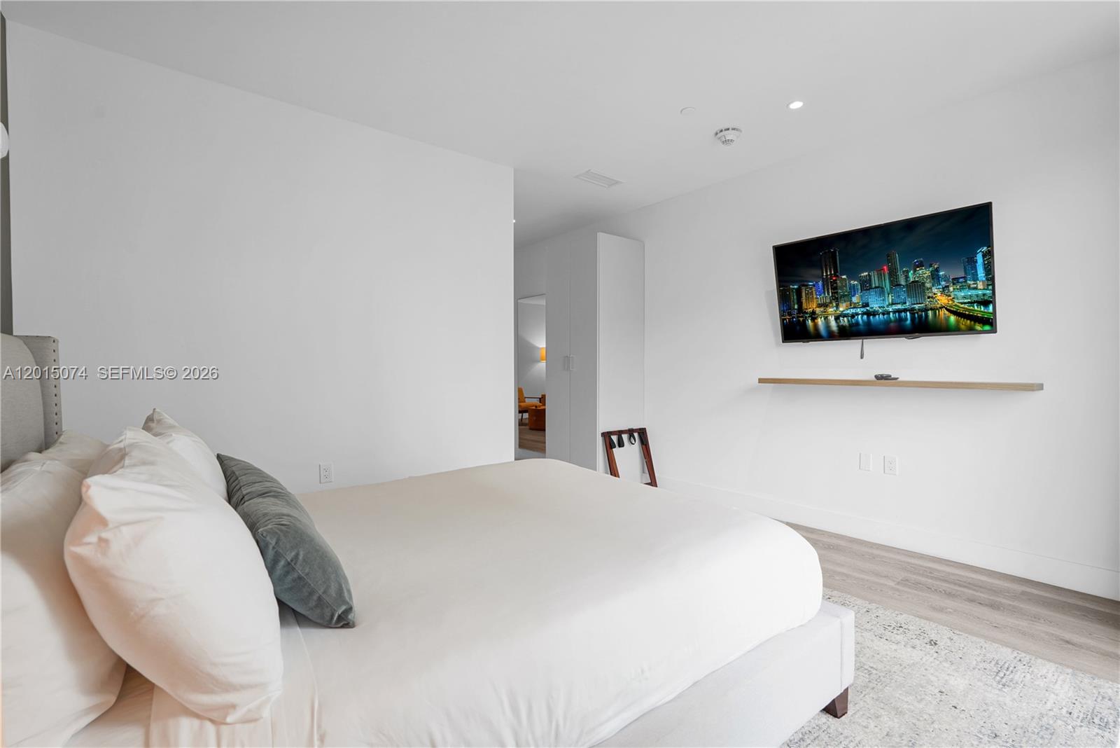 A bedroom features a bed, a wall-mounted television above a floating shelf, and white walls — 229 SW 9th St # 404, Miami FL 33130, MIAMI, FL
