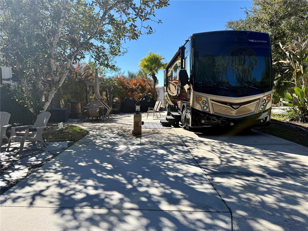 A large recreational vehicle is parked on a concrete driveway next to a paved patio — 124 STALLION LANE, LAKE WALES, FL